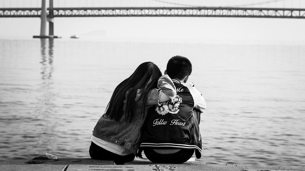 คู่รักนั่งใกล้กันริมทะเลสาบ